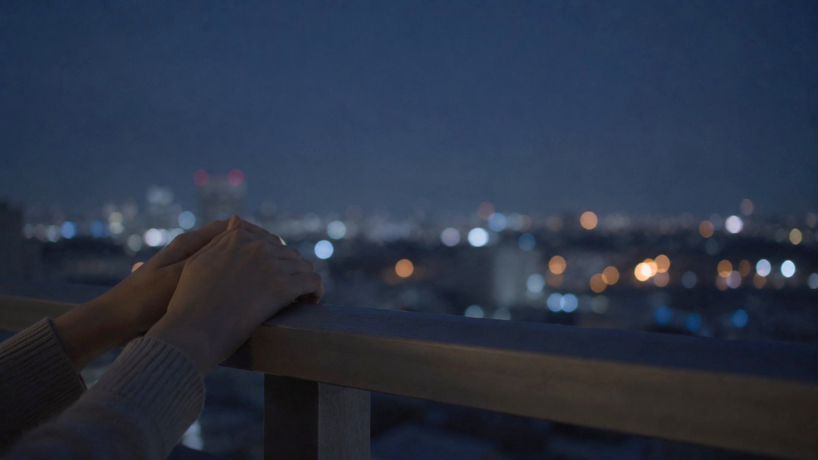 夜のベランダの手すりに置いた両手と遠い街の明かり