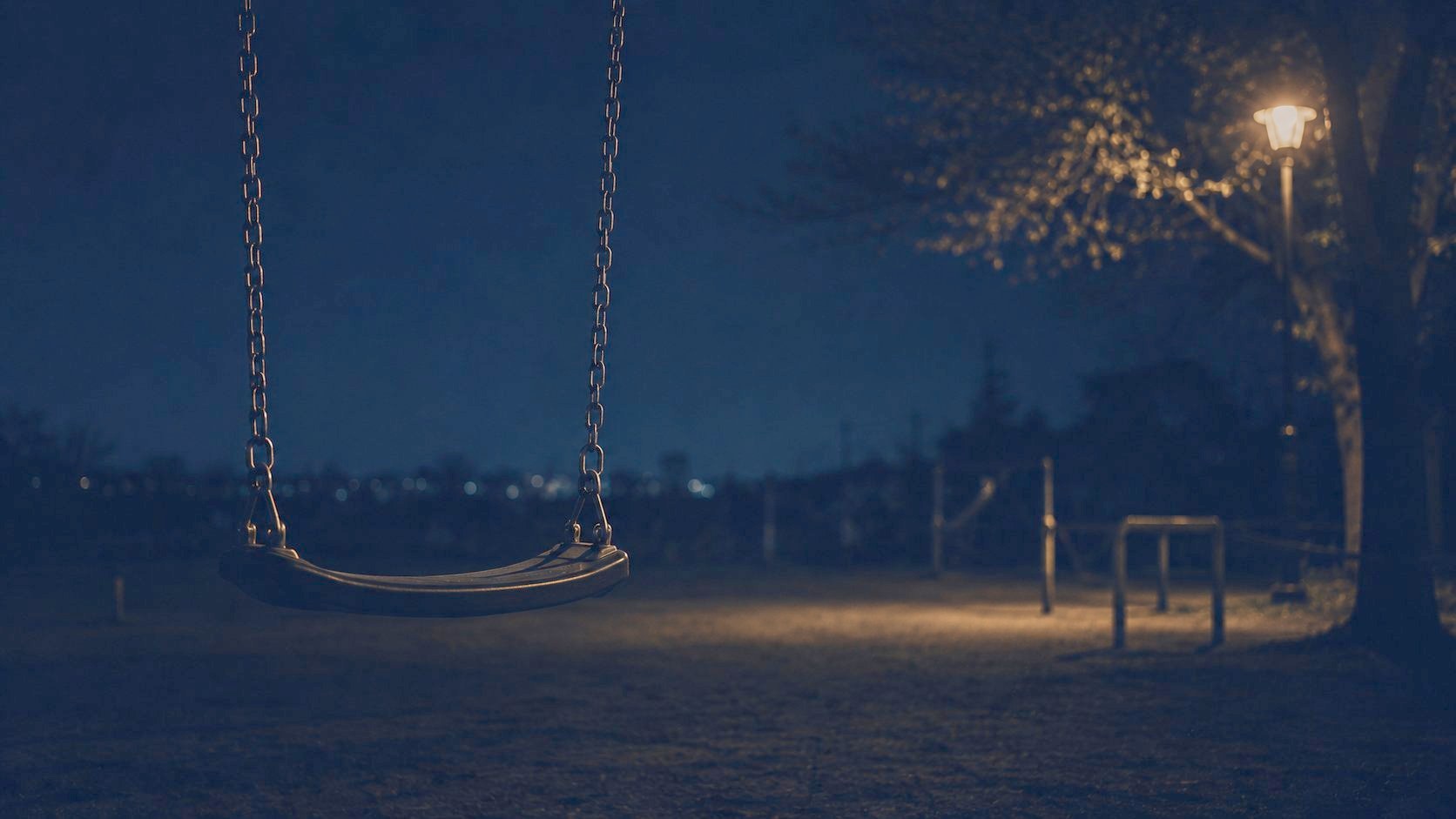 夜の公園で、誰もいないブランコが街灯に照らされている