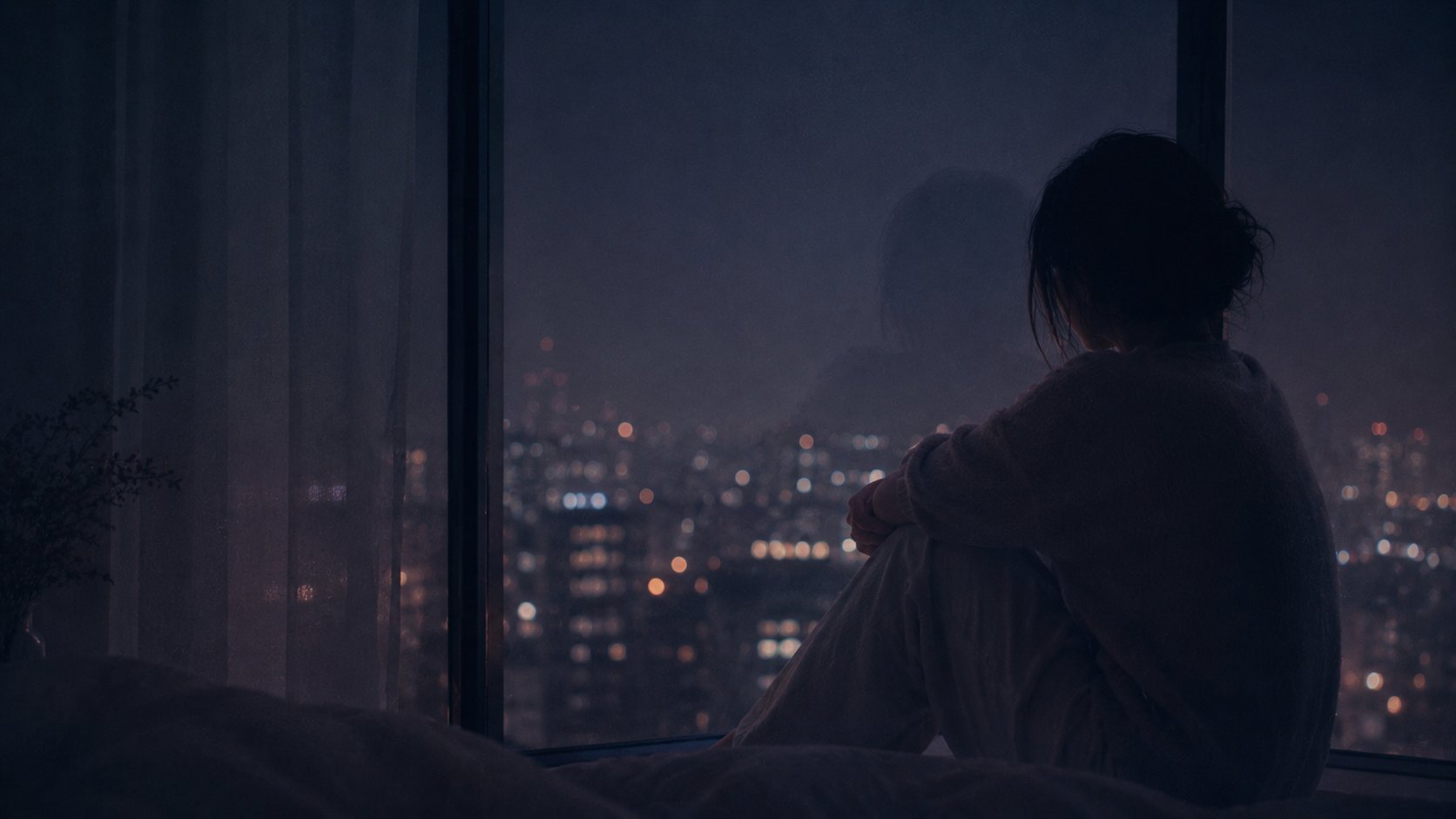 夜景の窓辺で膝を抱えて座る女性のシルエット
