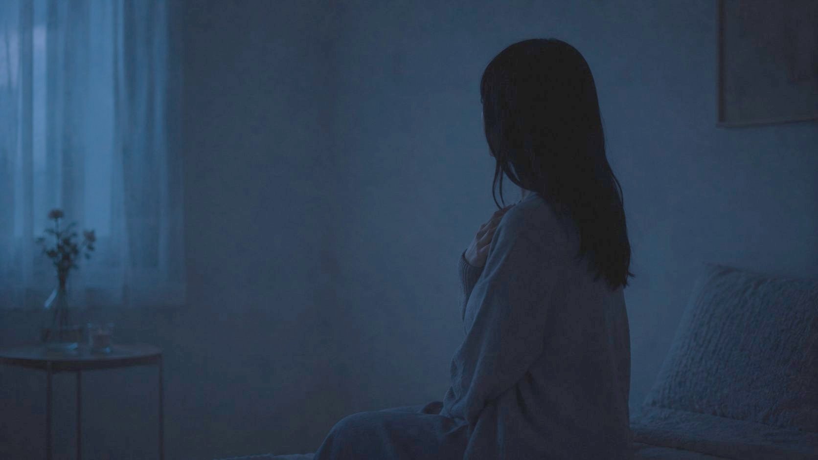 夜、ベッドの縁で胸に手を当てて座る姿