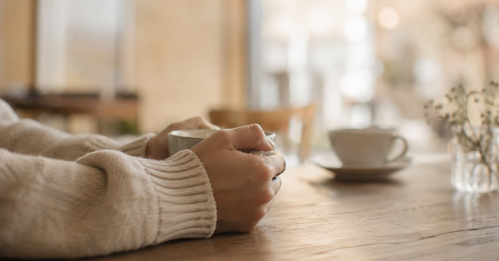 カフェのテーブルで、自分のカップを両手で固く握る手元